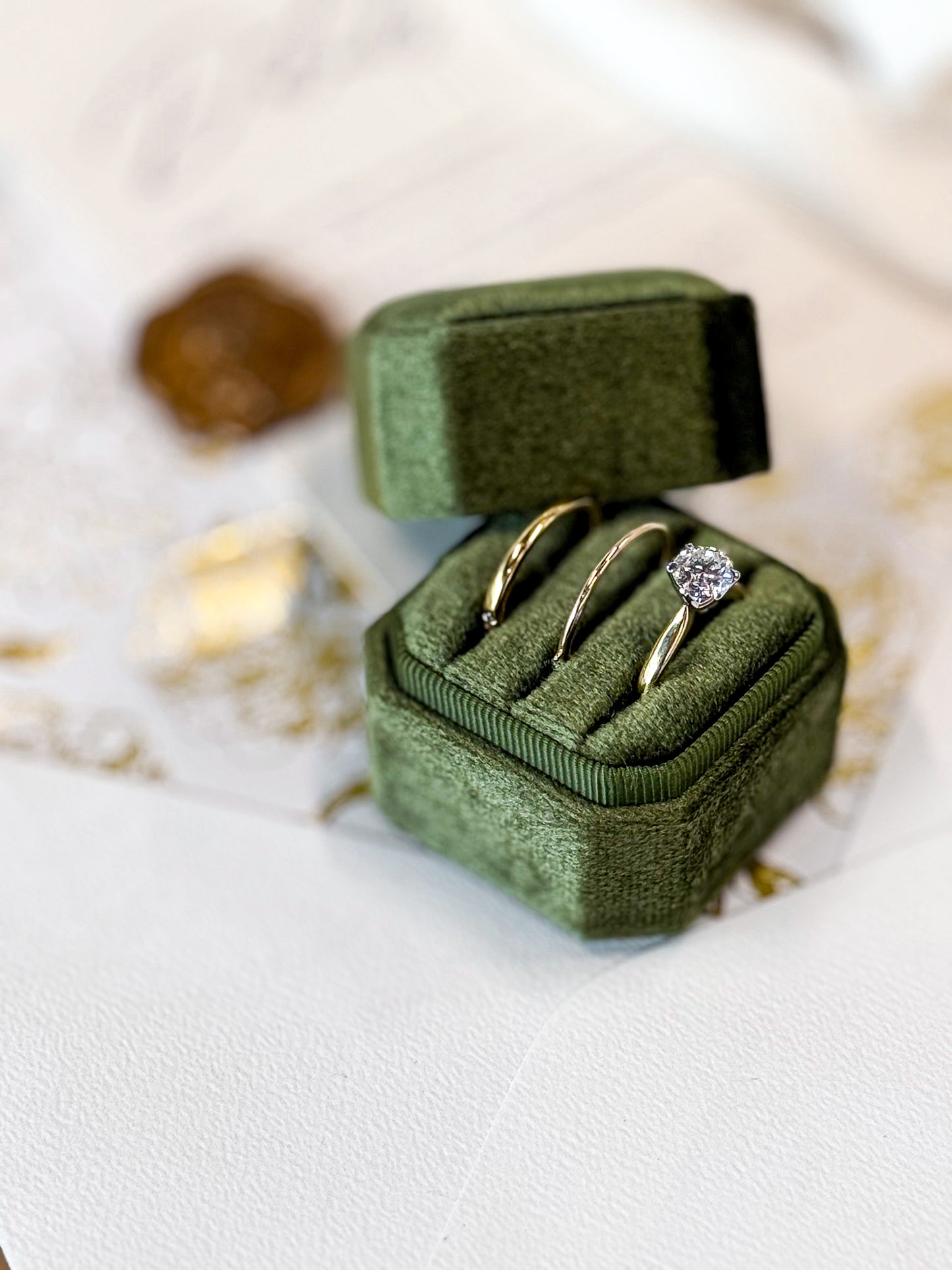 Green velvet ring box with two gold rings on a light background