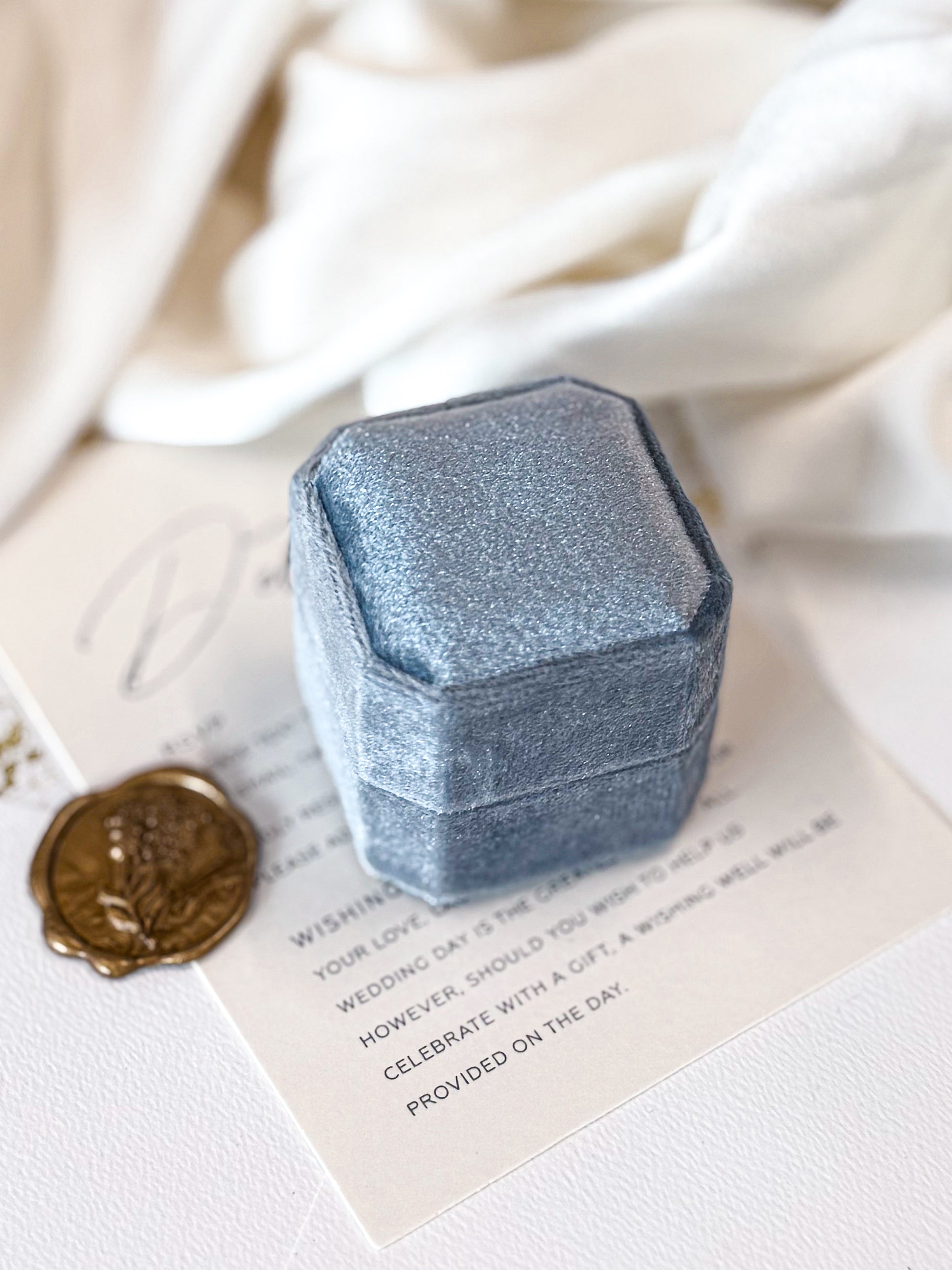 Blue jewelry box on a white surface with a wax seal and paper