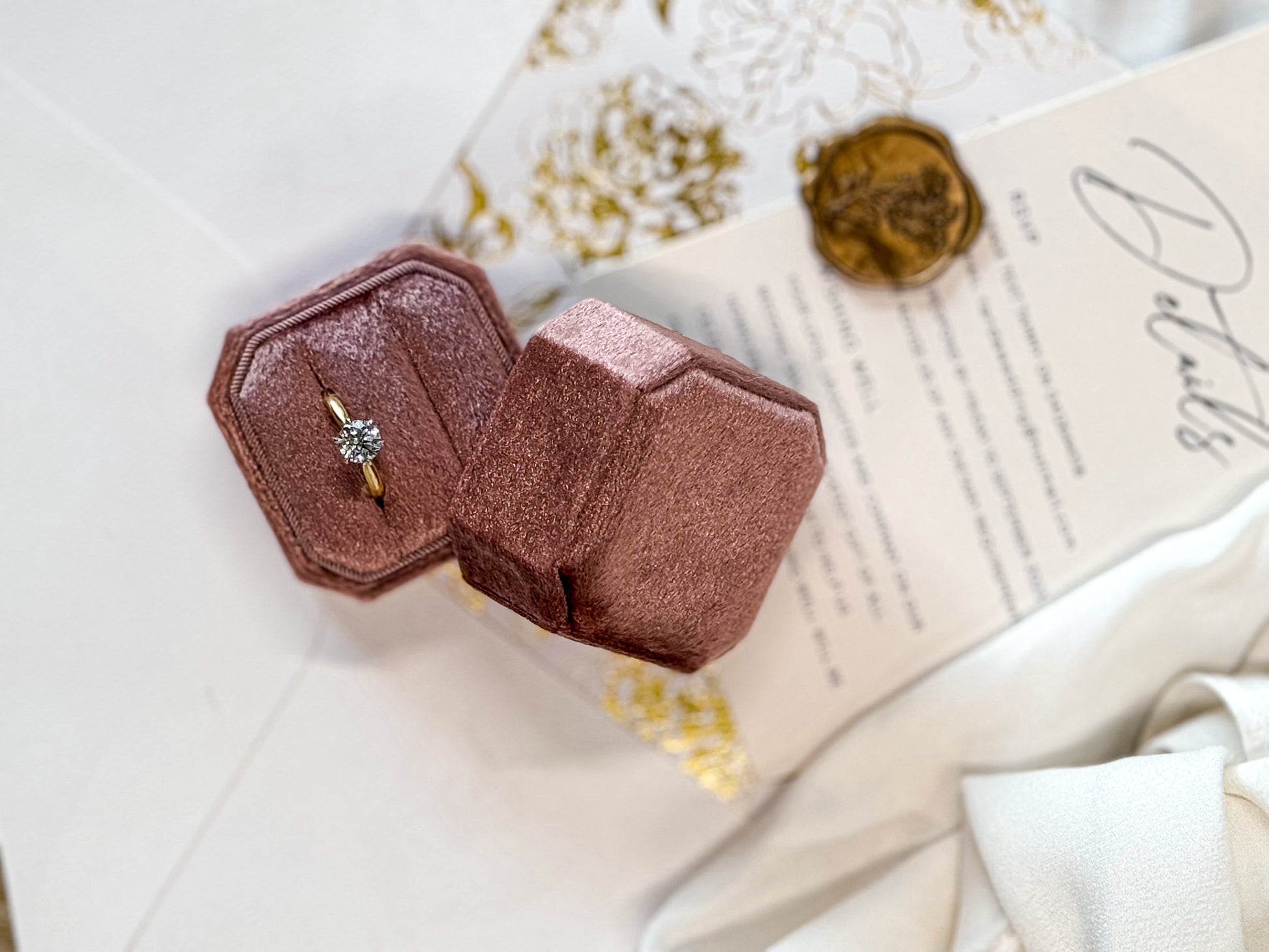 Rose gold ring box with a ring inside on a textured surface