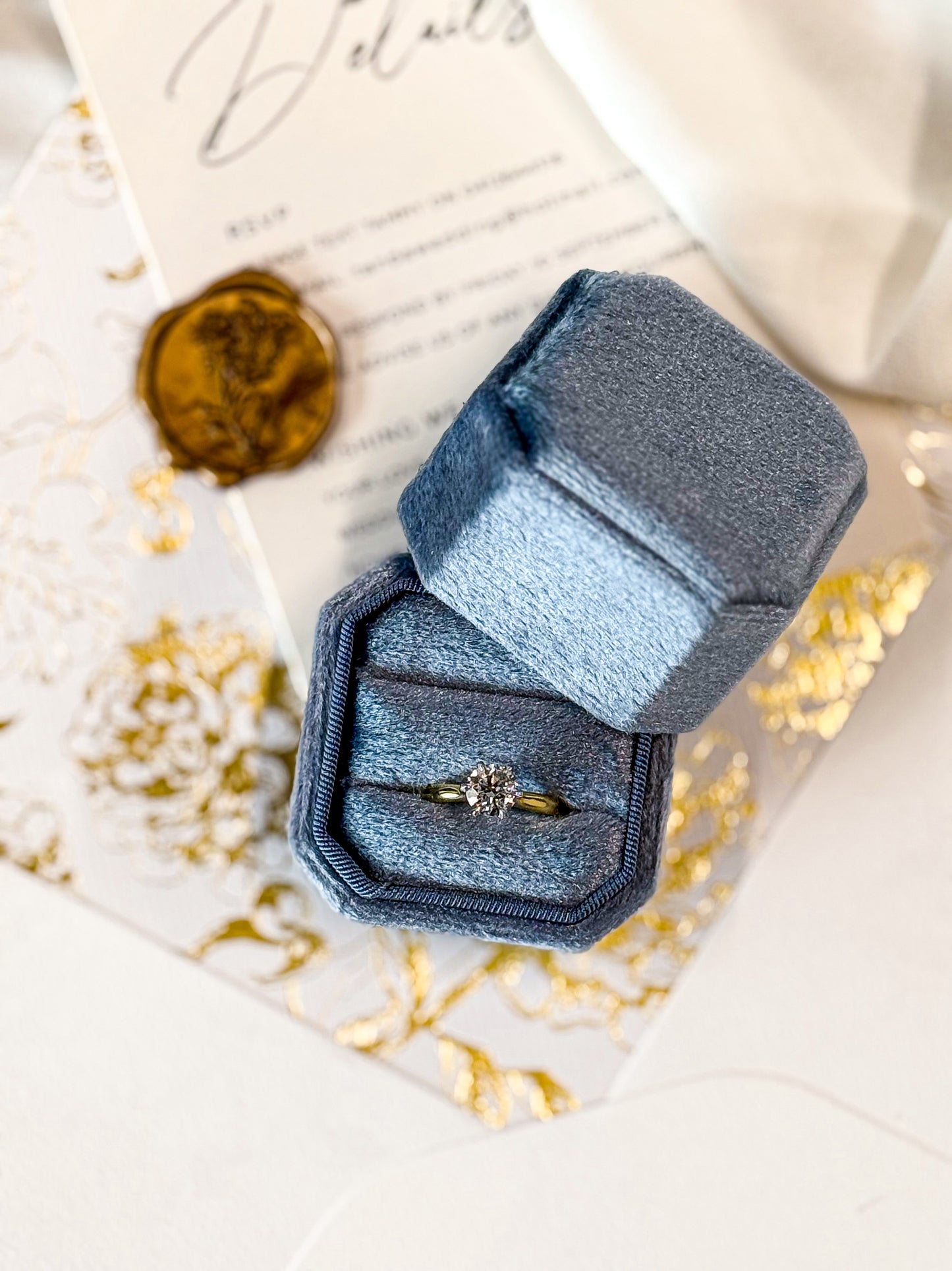 Blue velvet ring box with a ring on a decorative card with gold confetti