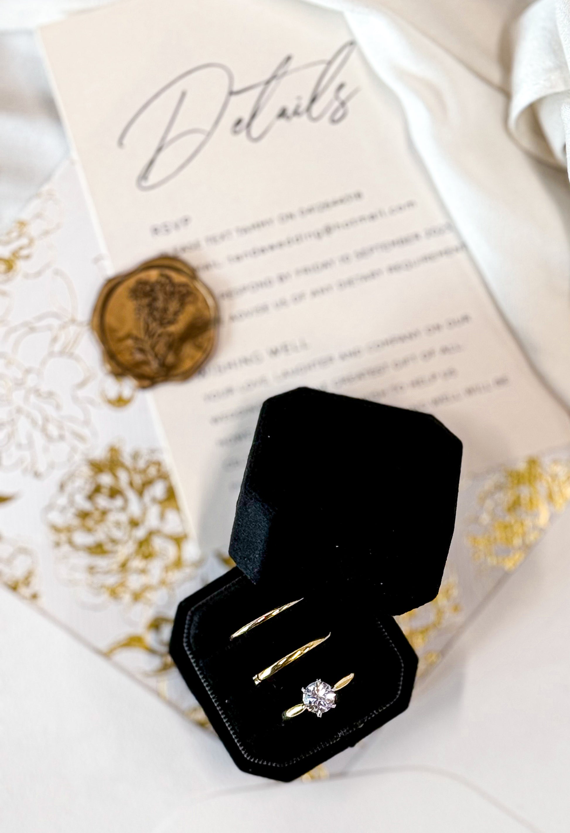 Black jewelry box with gold rings on a decorative paper background