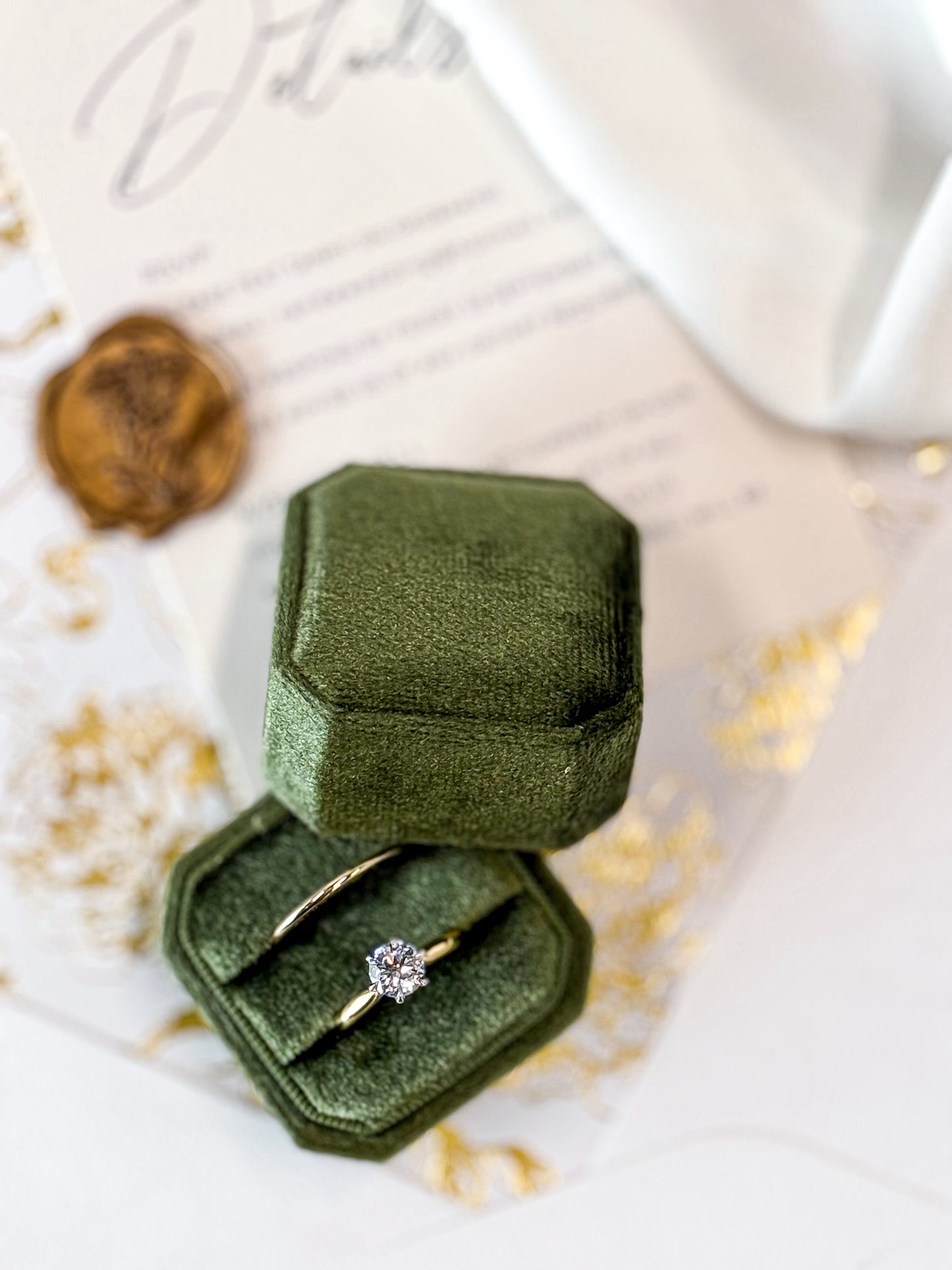 Green velvet ring box with a gold ring featuring a diamond on a light background
