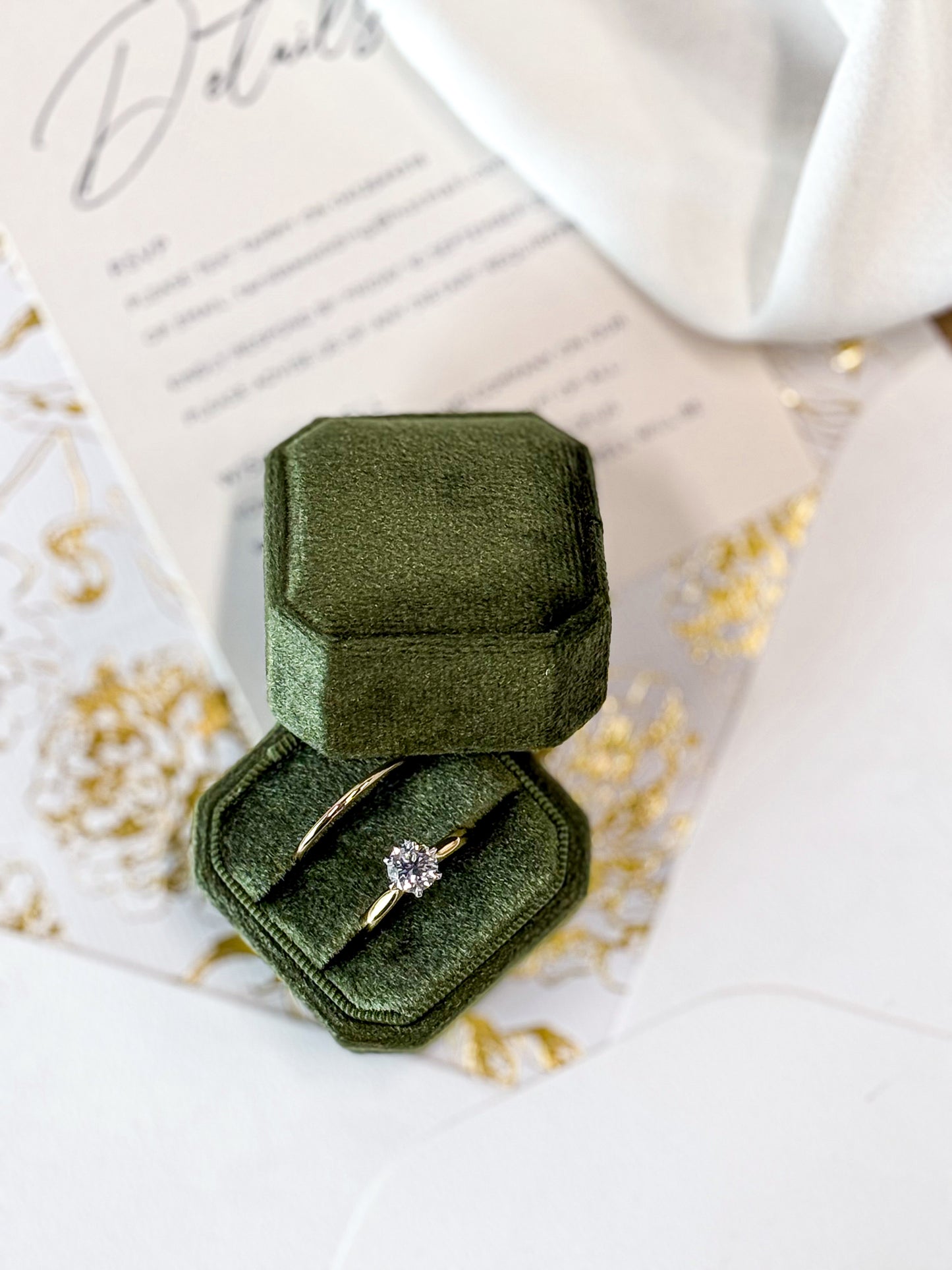 Green velvet ring box with a gold ring on a white surface with text