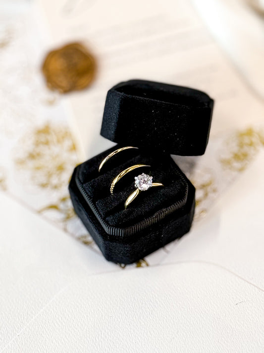Gold ring with a diamond in a black velvet box on a white surface.