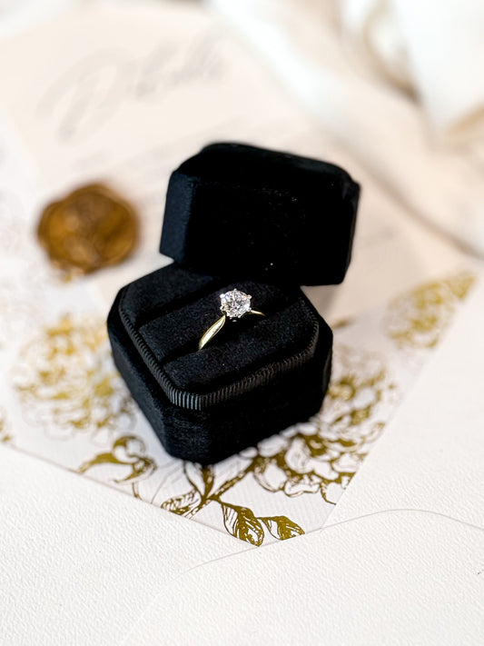 Diamond ring in a black velvet box on a decorative white and gold surface