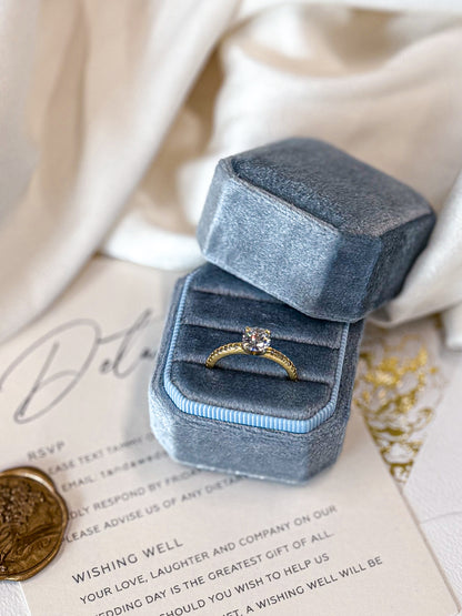 Blue velvet ring box with a gold ring on a white surface