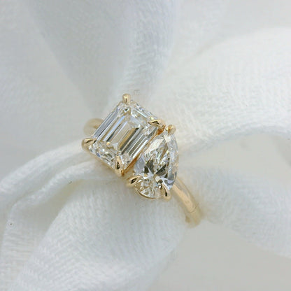 Diamond ring with emerald-cut and pear-shaped stones on a white fabric background