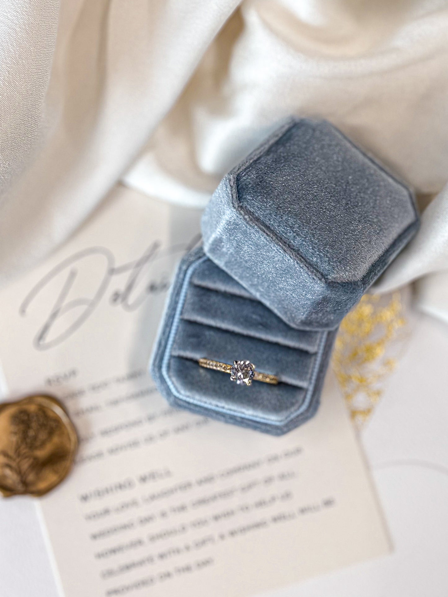 Blue velvet ring box with a ring on a piece of paper