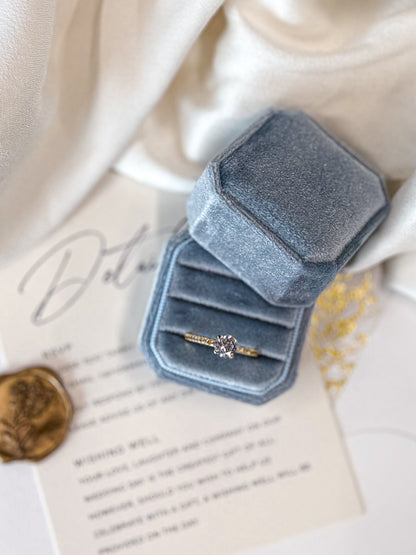 Blue velvet ring box with a ring on a piece of paper