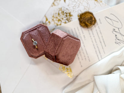 Rose gold ring box with a ring inside on a textured surface