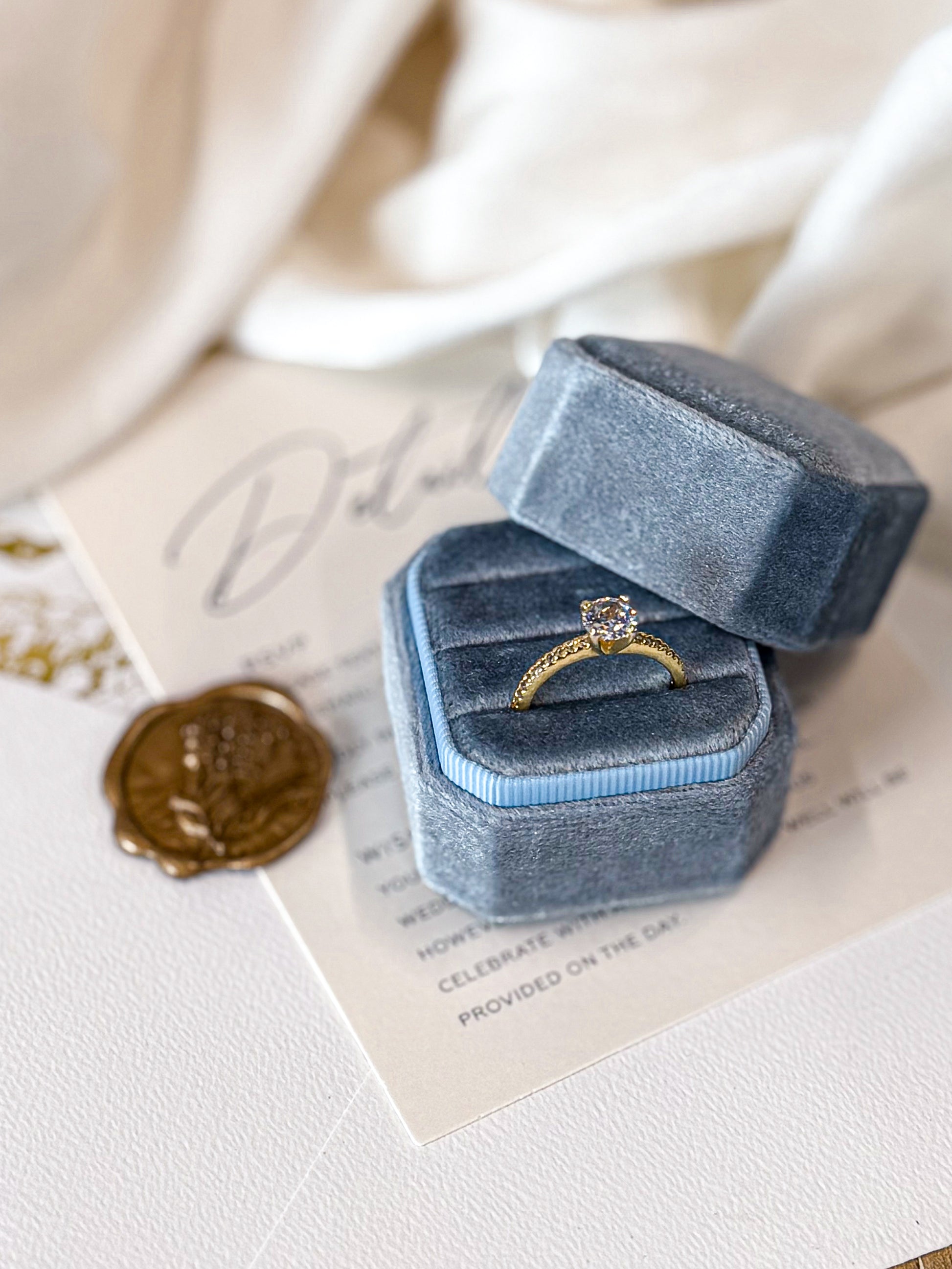 Blue velvet ring box with a gold ring on top of an old letter.