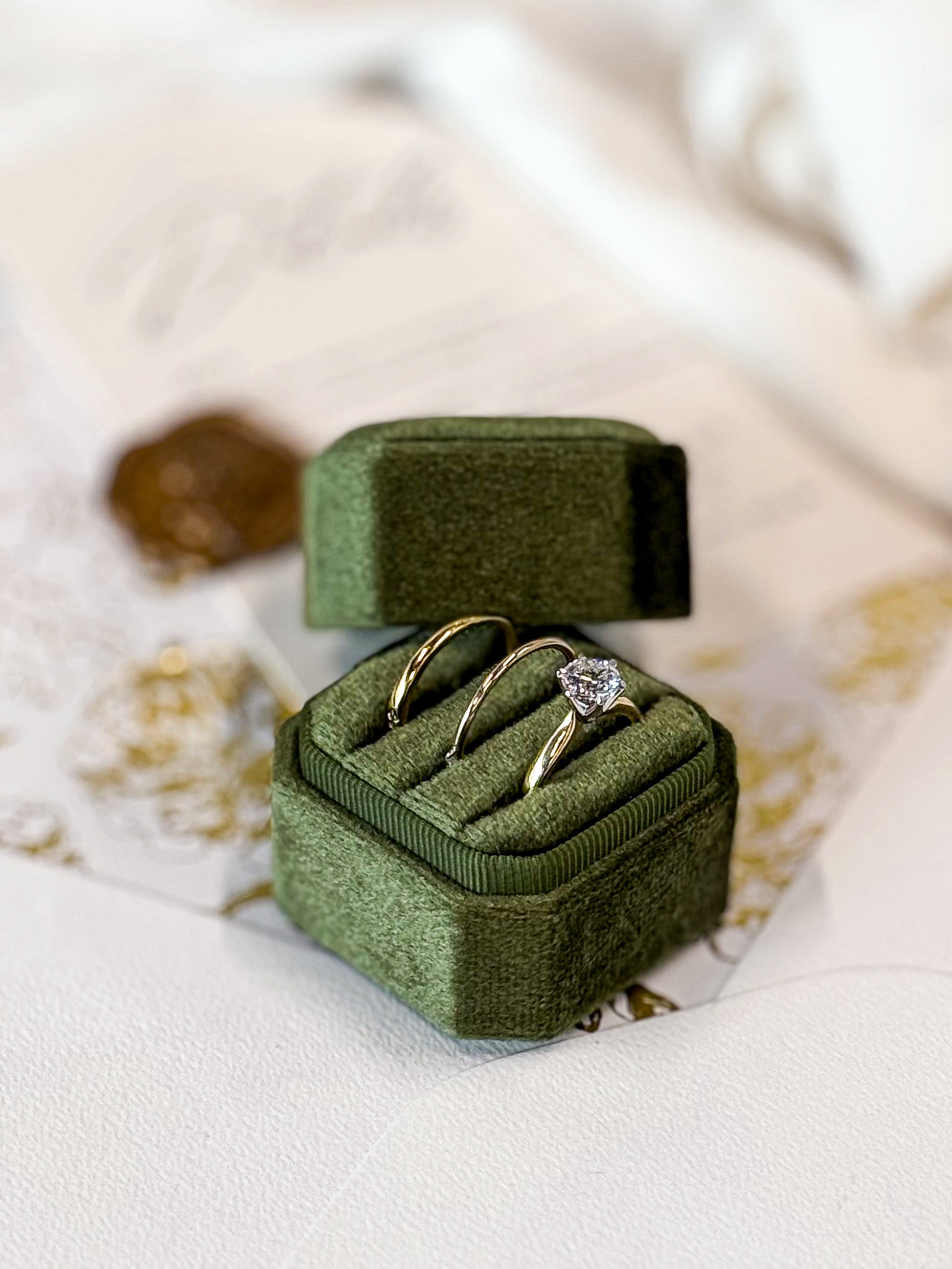THREE gold rings with a diamond in a green velvet box on a textured surface.