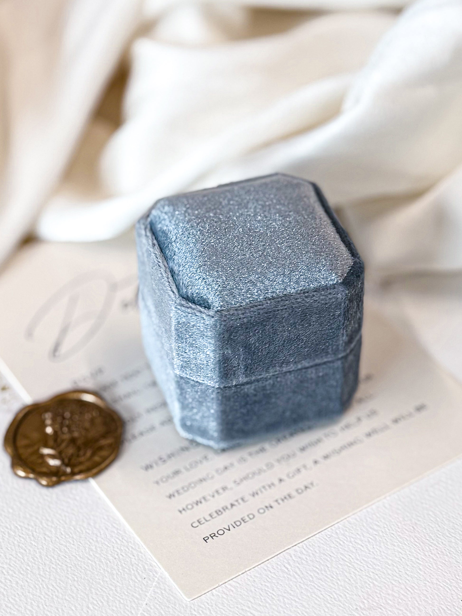 Blue velvet jewelry box on a white surface with a wax seal