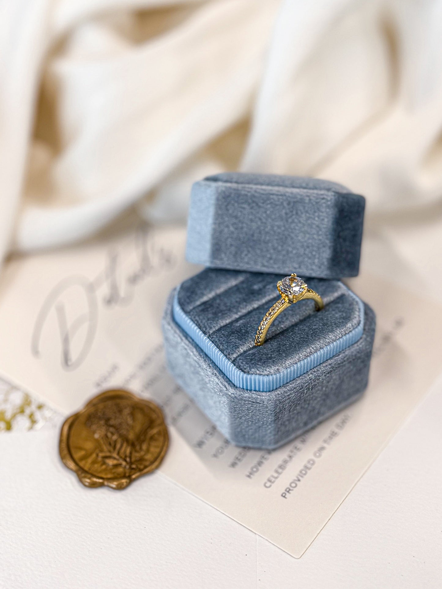 Blue velvet ring box with a gold ring on a white surface