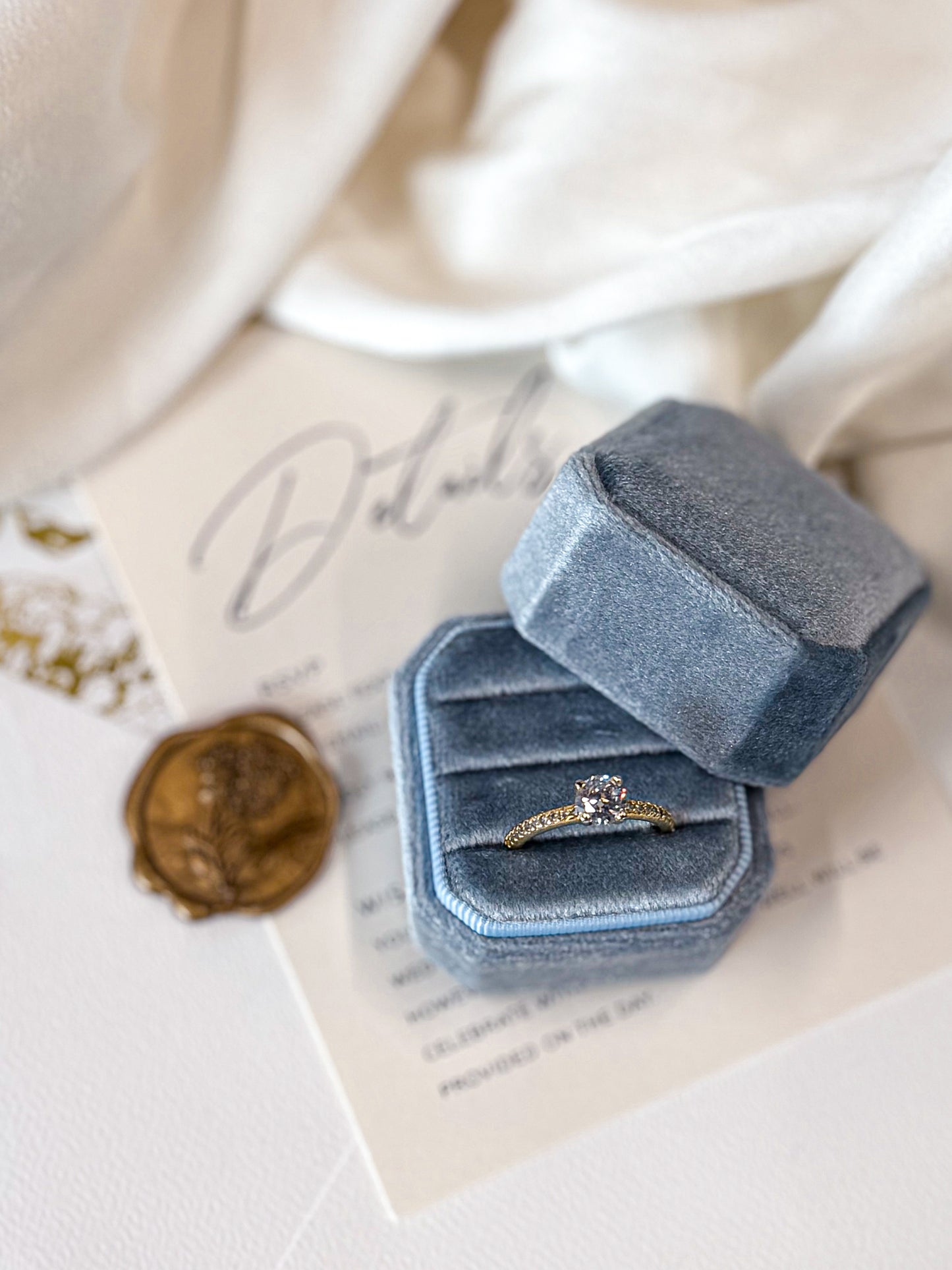 Blue velvet ring box with a gold ring on a white surface