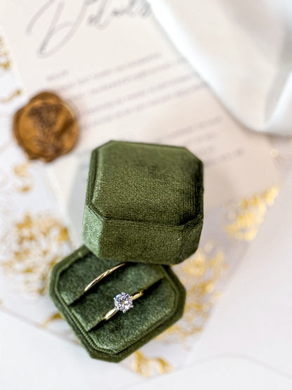 Green velvet ring box with a gold ring featuring a diamond on a white surface.
