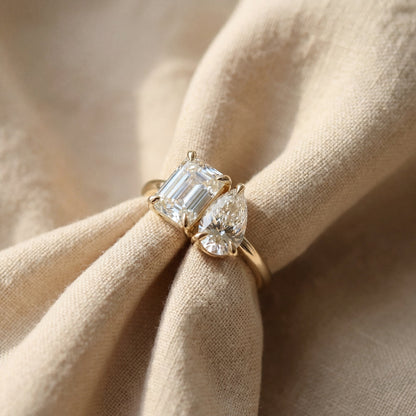 Gold ring with emerald-cut and pear-shaped diamonds on beige fabric