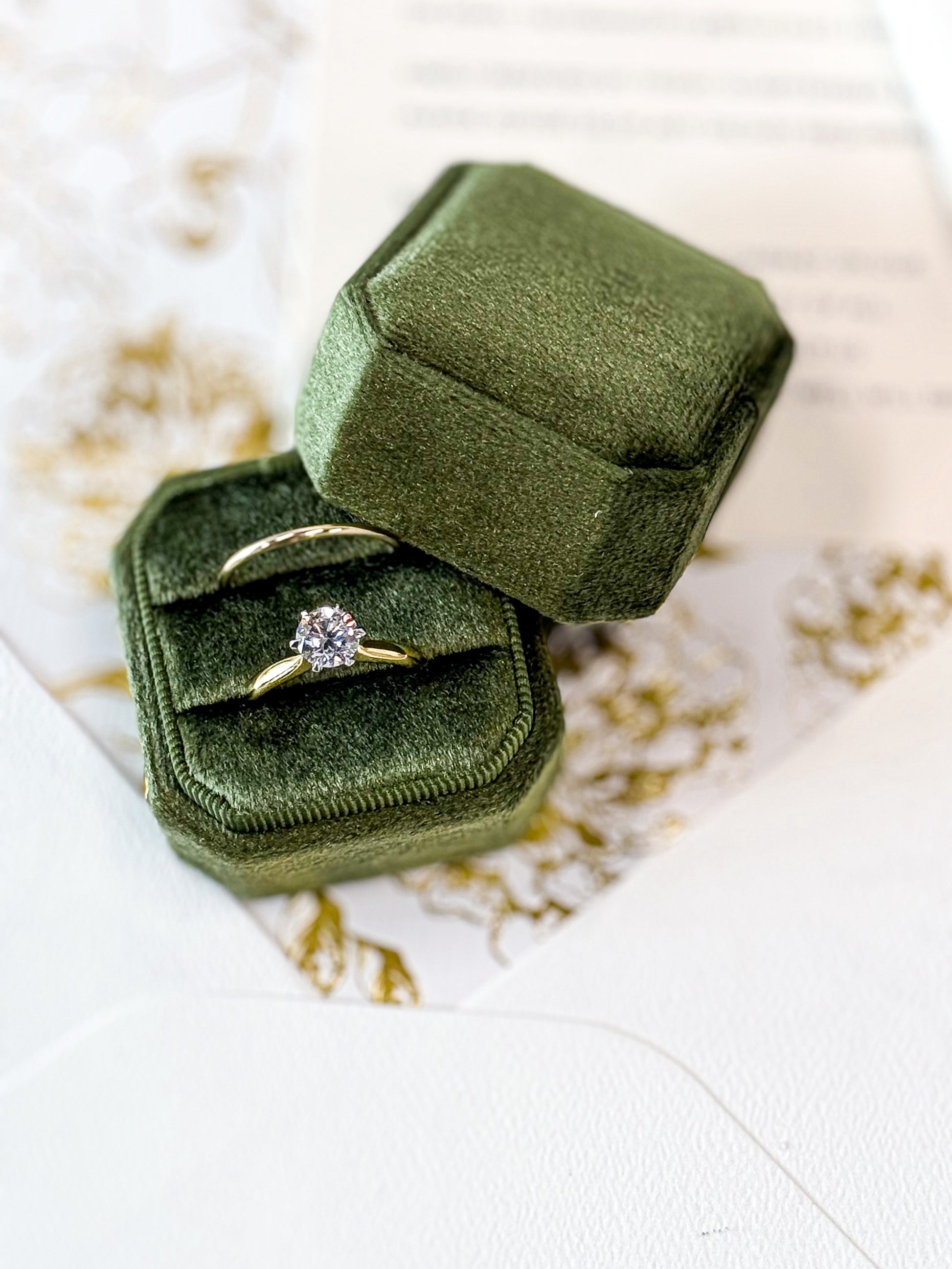 Gold ring with a diamond in a green velvet box on a white surface with gold leaf