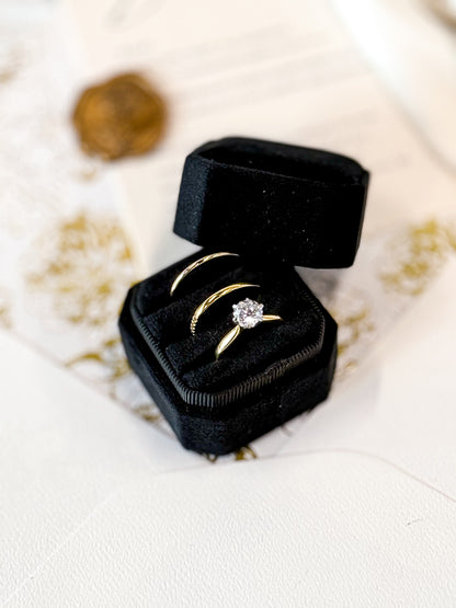Gold ring with a diamond in a black velvet box on a white surface.